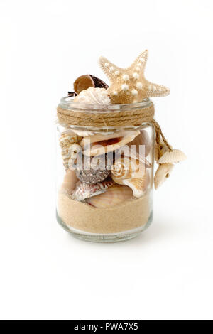 Vielzahl von Muscheln und Sand in einer handgefertigten Glas Glas mit mini Muscheln dekoriert und auf weißem Hintergrund. Low Angle View. Stockfoto