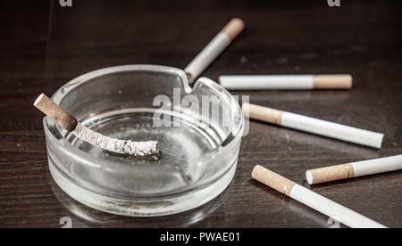 Einer glimmenden Zigarette brennt in einem Aschenbecher auf dem Tisch mit Zigaretten um Sie herum Stockfoto