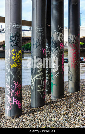 Graffiti-bedeckten Säulen unter dem Festival Pier bei Ebbe auf der Themse Ufer, London, UK Stockfoto