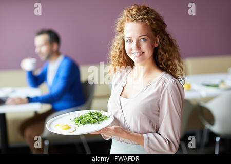 Lächelnden jungen hübschen Kellnerin Halteplatte mit frische Mahlzeit für einen Kunden Stockfoto