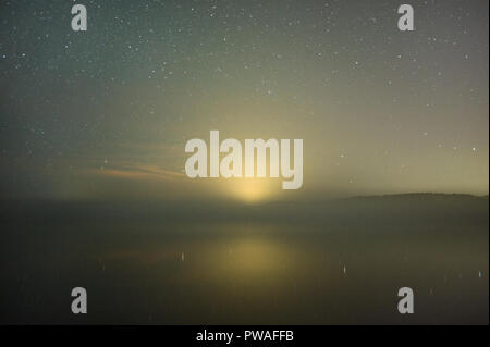 Sternenhimmel über misty See. Stadt Lichtverschmutzung in Horizont. Stockfoto