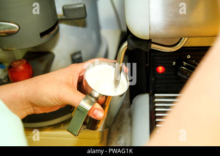 Frauen machen Aufschäumen der Milch in eine Kaffeemaschine in bar an. Nahaufnahme der kaukasischen Frau barista Hände halten Milchkännchen für die Zubereitung von Kaffee mit Kaffeemaschine. Stockfoto
