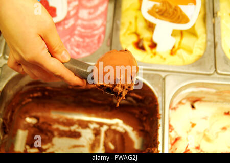 Weibliche hand mit Schaufel nimmt Eis Schokolade aus dem Kühlschrank und im Waffle Kegel dienen. Frau, die Kugel leckeres Eis. Stockfoto
