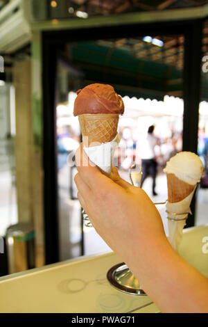 Die weibliche Hand hält Eis in der Ecke. Eis in der Waffel Kegel. Kühlschrank mit Eis im Hintergrund. Frau arbeitet in der Eisdiele. Stockfoto