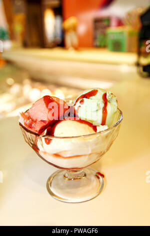 Weibliche Verkäufer gießt Soße auf Eis. Frau schwer machen Eis Kupfer Schale mit Obst und Süßigkeiten schmilzt in ein hohes Becherglas. Stockfoto