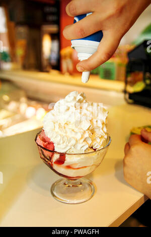 Weibliche Verkäufer gießt Soße auf Eis. Frau schwer machen Eis Kupfer Schale mit Obst und Süßigkeiten schmilzt in ein hohes Becherglas. Stockfoto