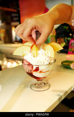 Weibliche Verkäufer gießt Soße auf Eis. Frau schwer machen Eis Kupfer Schale mit Obst und Süßigkeiten schmilzt in ein hohes Becherglas. Stockfoto