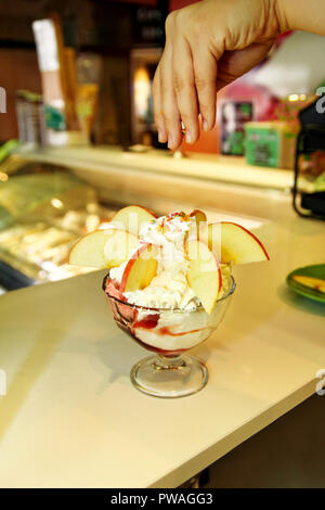 Weibliche Verkäufer gießt Soße auf Eis. Frau schwer machen Eis Kupfer Schale mit Obst und Süßigkeiten schmilzt in ein hohes Becherglas. Stockfoto