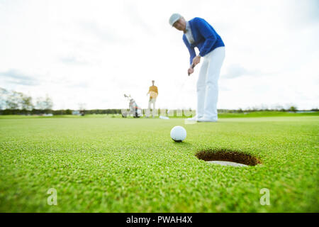 Golf Ball in der Nähe des Loch im Boden auf dem Hintergrund der Golf Player gehen Sie zu schlagen Stockfoto