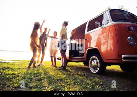 Sommer Urlaub, Reise, Urlaub, Reisen und Menschen Konzept - lächelnden Jungen hippie Freunde Spaß über minivan Auto Stockfoto