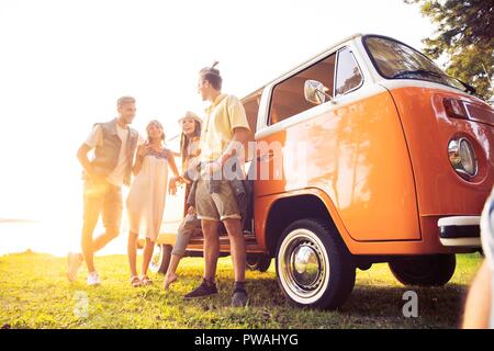 Sommer Urlaub, Reise, Urlaub, Reisen und Menschen Konzept - lächelnden Jungen hippie Freunde Spaß über minivan Auto. Stockfoto