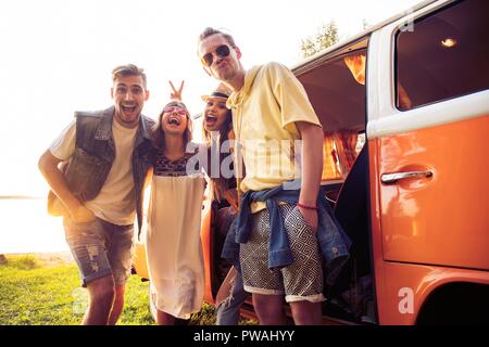 Sommer Urlaub, Reise, Urlaub, Reisen und Menschen Konzept - lächelnden Jungen hippie Freunde Spaß über minivan Auto. Stockfoto