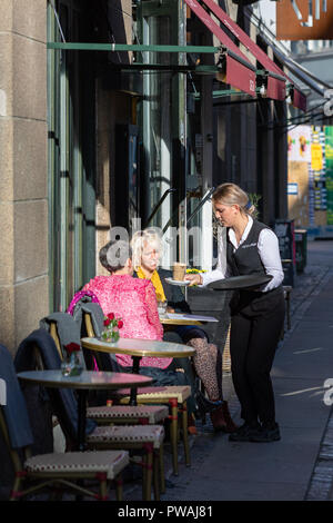 Kellnerin Kaffee für zwei Frauen vor einem Cafe in einer kleinen Straße in Kopenhagen, Dänemark, sitzen Stockfoto