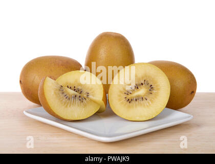 Sungold Kiwi in der Hälfte mit ganzen Früchten hinter auf weiße Platte auf Holz Tisch geschnitten. Im Gegensatz zu den Grünen Kiwis, Neue SunGold Kiwis haben eine glatte Haut Stockfoto