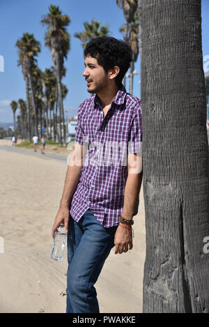 Ein hübscher junger Mann gegen eine Palme am Strand schiefen Stockfoto