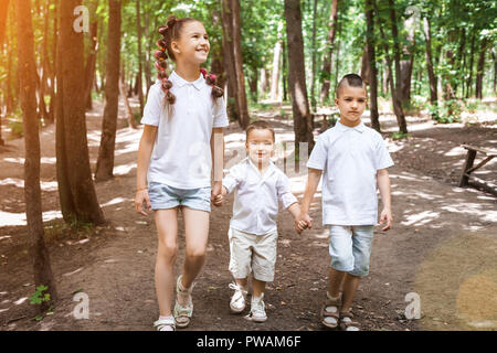 Glückliche Kinder tragen weiße Hemden im sonnigen Wald. Nettes Mädchen ist Laufen mit ihren kleinen Brüdern. Konzept von Liebe und Familie Stockfoto