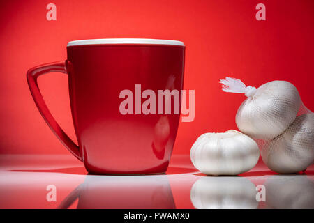 Rot Tasse mit kleiner Haufen von Knoblauch auf dem roten Hintergrund isoliert Stockfoto