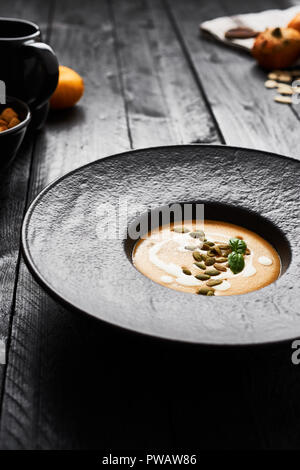 Kürbis und Karotten Suppe mit Kürbiskernen, Sahne und Basilikum in Schwarz moderne Platte auf dunklen Holztisch mit kopieren. Dunklen modernen Stil. Stockfoto