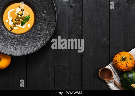 Kürbis und Karotten Suppe mit Kürbiskernen, Sahne und Basilikum auf dunklem Hintergrund mit kopieren. Ansicht von oben. Stockfoto