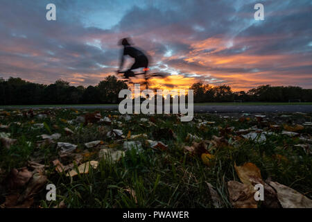 Radfahren in einem dramatischen herbstlicher Sonnenuntergang in einem Londoner Park am Ende des Tages Stockfoto