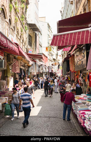 Reihen von Läden mit Waren auf Zeile einer hügeligen Straße mit Kopfsteinpflaster mit Menschen und Touristen spazieren im Stadtteil Fatih, Istanbul, Türkei Stockfoto