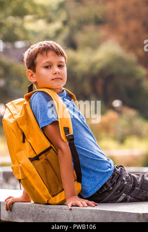 Kind mit Rucksack Sitzen im Freien und Blick in die Kamera Stockfoto