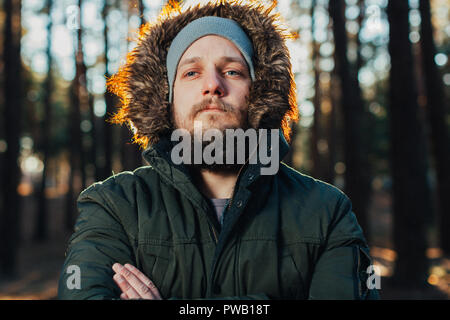 Porträt, Nahaufnahme der Jungen stilvoll ernster Mann mit Bart in rgreen Winter Jacke mit Kapuze und Fell auf dem Kopf bekleidet steht gegen die Rückseite Stockfoto