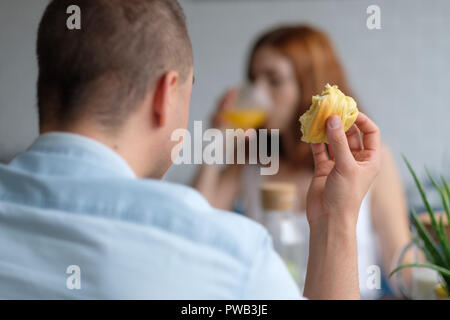 Selektiver Fokus Foto von zwei Menschen ein Croissant essen und trinken Orangensaft zum Frühstück Stockfoto