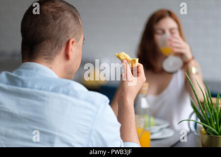 Selektiver Fokus Foto von zwei Menschen ein Croissant essen und trinken Orangensaft zum Frühstück Stockfoto