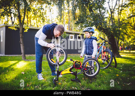 Vatertag kaukasischen Papa und unseren 5 Jahre alten Sohn im Hinterhof in der Nähe des Hauses auf dem grünen Rasen auf dem Rasen Reparatur Fahrrad, pumpt ein Fahrrad whe Stockfoto