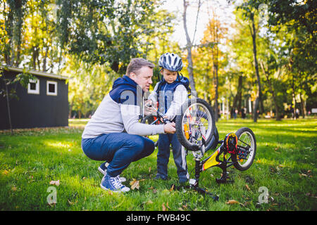 Vatertag kaukasischen Papa und unseren 5 Jahre alten Sohn im Hinterhof in der Nähe des Hauses auf dem grünen Rasen auf dem Rasen Reparatur Fahrrad, pumpt ein Fahrrad whe Stockfoto