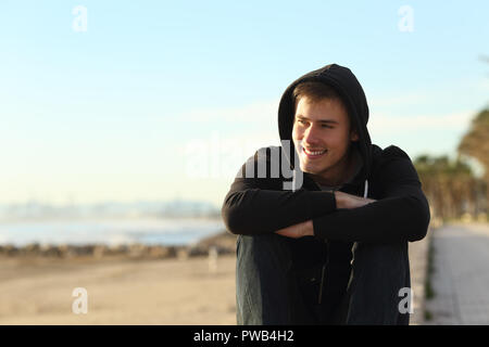 Vorderansicht Porträt eines Teenager-Jungen sitzen am Strand entfernt suchen Stockfoto