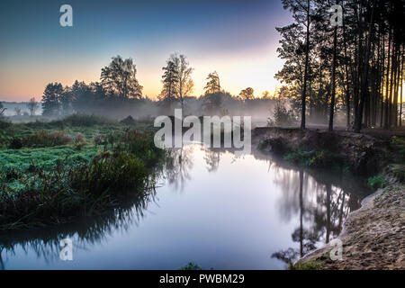 Fluss im Nebel, kurz vor Sonnenaufgang. Ein warmes Glühen in den Wolken von den ersten Strahlen der Sonne. Stockfoto