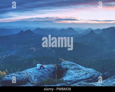 Müde tourist sitzt auf der Kante einer Klippe in die Ferne schauen. Wanderer ruht auf Mountain Trail. Unglaubliche Aussicht vom Gipfel. Stockfoto