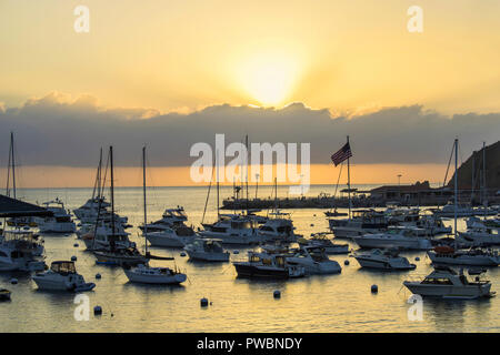 Mit Sonnenstrahlen über Hafen voller Boote mit orange Licht reflektieren auf ocean Oberfläche und die amerikanische Flagge auf dem Horizont Daybreak Stockfoto