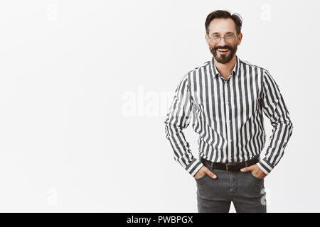 Mann in formalen Outfit gekleidet, bereit, Partei zu kommen. Portrait von gut aussehenden freundlichen und fröhlichen Art Mann mit Bart in Gläsern, Hände in den Taschen und breit grinsend mit zuversichtlichem Blick Stockfoto