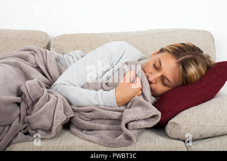 Kranke junge Frau auf der Couch liegen in einem grauen Decke gewickelt Stockfoto