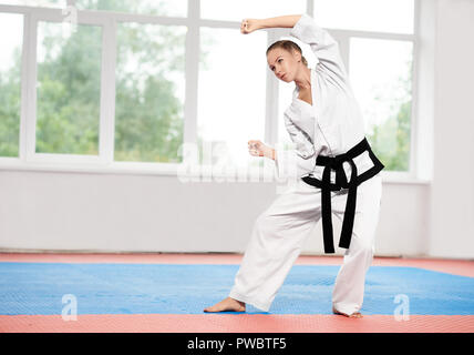Blonde Mädchen tragen in weißen Kimono mit schwarzen Gürtel in Karate Kampfkunst zu üben. Professionelle Kämpferin perfektionierung Karate position Qualität der Schlacht zu verbessern. Konzept der Sport. Stockfoto