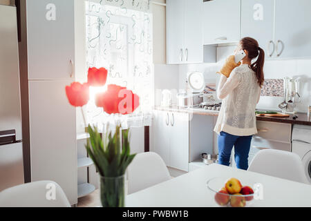 Kochen Frau Abendessen im neuen Küche und am Telefon zu sprechen. Moderne Küche Design. Weiße und graue sauber Esszimmer Stockfoto