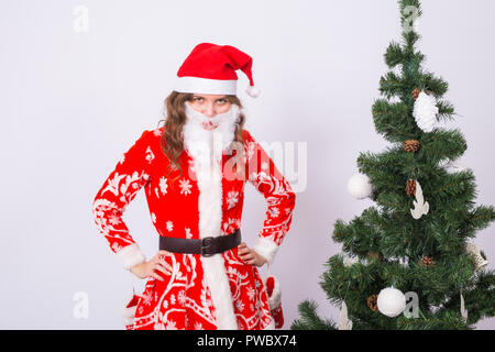 Urlaub, Weihnachten und Witz Konzept - lustige Frau in Santa Kostüm mit falschen Bart in der Nähe von Weihnachten Baum auf weißem Hintergrund Stockfoto