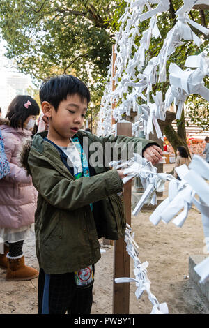 Japanische neues Jahr, shogatsu. Junges Kind, Junge, Binden schlechtes Vermögen Papierstreifen, Omikuji zu rahmen Pech hinter an der Nishinomiya Schrein zu verlassen. Stockfoto