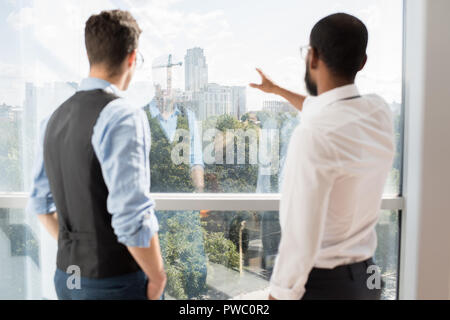 Ansicht der Rückseite des Bauleiter in formale stehend an Fenster und diskutieren neue Gebäude, während die weitere Arbeit planen Stockfoto