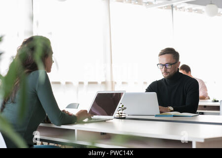 Büros von Mitarbeitern mit tragbaren Computern in der modernen offenen Raum: Konzentriert gut aussehender Geschäftsmann in Gläsern sitzen am Tisch und Analysieren von Daten Stockfoto