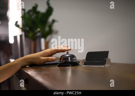 Close up Frauen rufen Sie das Hotel an der Rezeption auf dem Schreibtisch mit dem Finger drücken Sie eine Glocke in der Lobby Hotel. hotel Konzept. Stockfoto