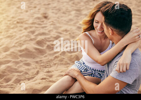 Romantische junge Paar Arm in Arm zusammen am Strand den Sonnenuntergang zu beobachten. Stockfoto
