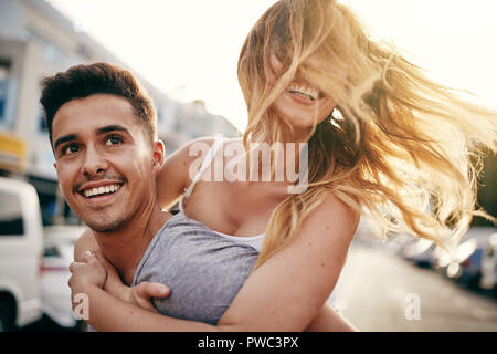Lachende junge Frau, die von ihrem Freund trug, und genießen Sie einen Tag in der Stadt Stockfoto