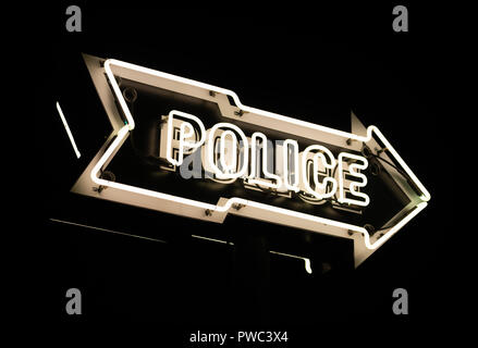 Es ist ein dunkler Himmel hinter einer einfachen weißen Neon Pfeil mit dem Wort Polizei in Großbuchstaben. Stockfoto