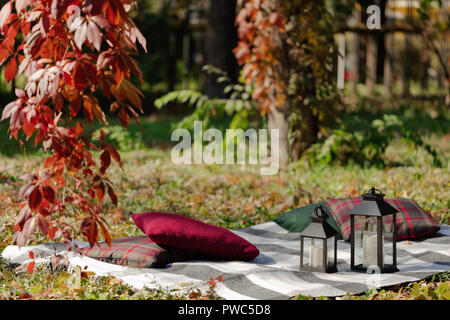 Herbst warme Tage. Indian Summer. Picknick im Garten - Decke und Kissen von Grau, Burgund und Grün Farbe auf dem Hintergrund der Blätter im Herbst. Sele Stockfoto