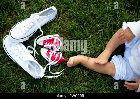 Red baby Kleinkinder Turnschuhe und weiße Frau Sneakers auf dem Gras mit kleinen Babys Füße Stockfoto