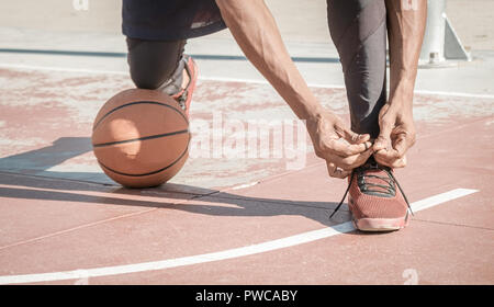 Eine afroamerican junger Mann ohne T-Shirt ist Basketball spielen in einem Park in Madrid im Sommer mittags. Er ist auf seine Knie, seine Schuhe binden mit t Stockfoto